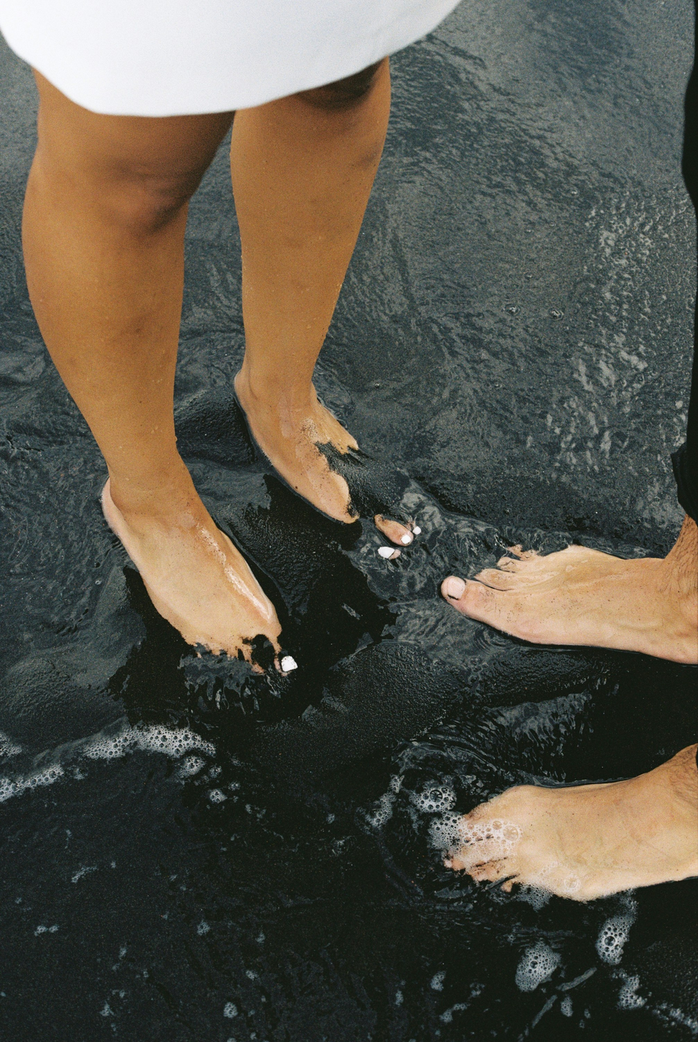 Couple's feet in water on a beach.