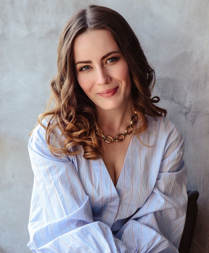 Smiling woman in blue blouse with curly hair.